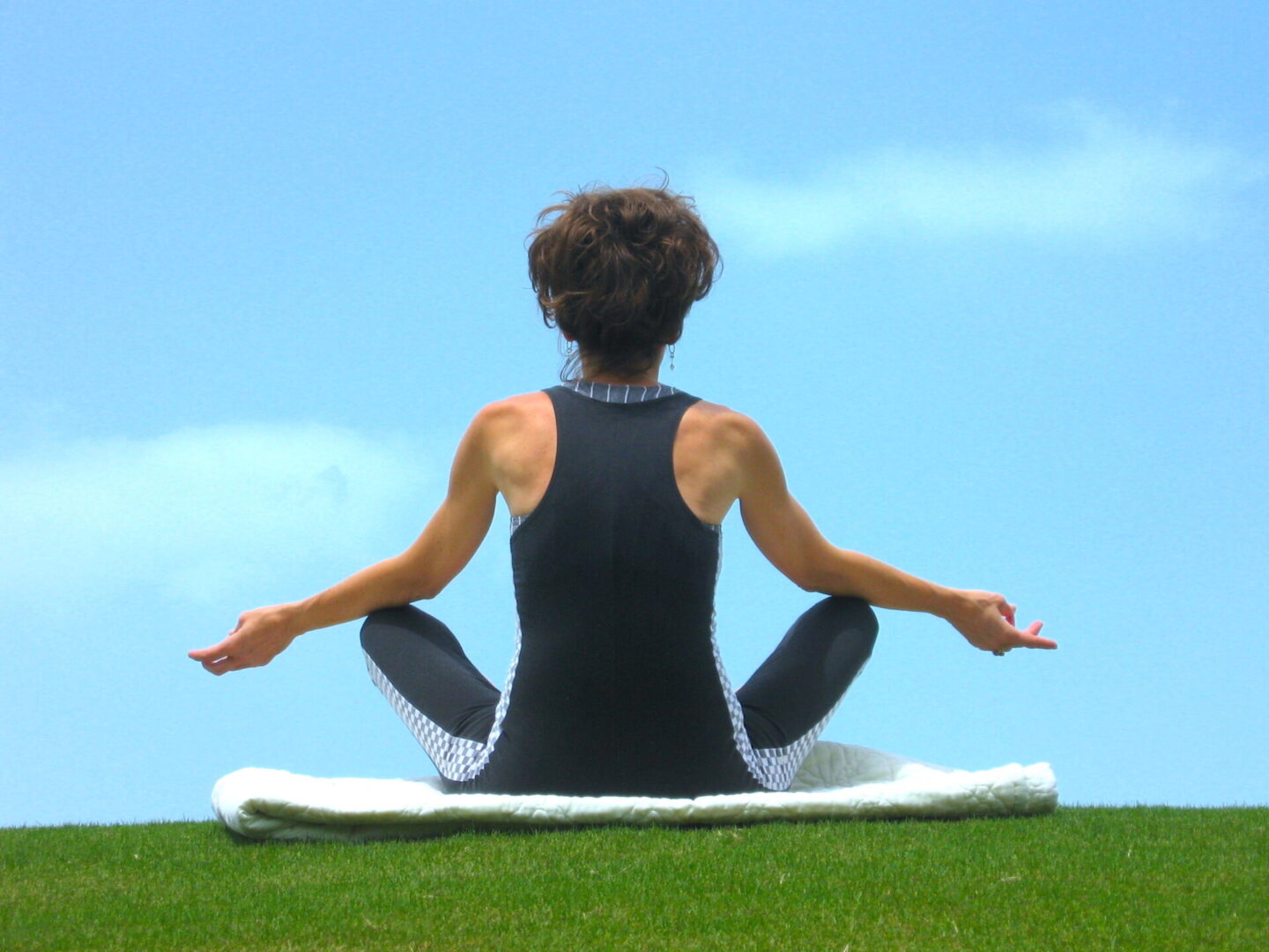 A woman sitting on the grass doing yoga.